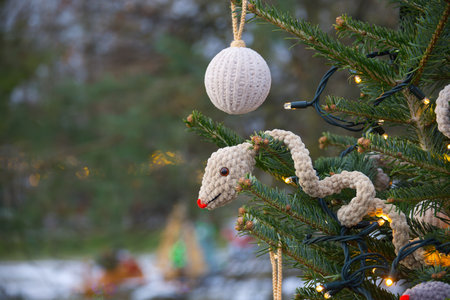 A festive Christmas tree with unique handmade ornaments, including a crochet snake and a round decoration, illuminated by warm string lights in an outdoor wintery setting.の写真素材