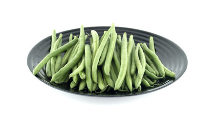 Fresh green beans arranged on a sleek black plate create a vibrant contrast against a clean white...