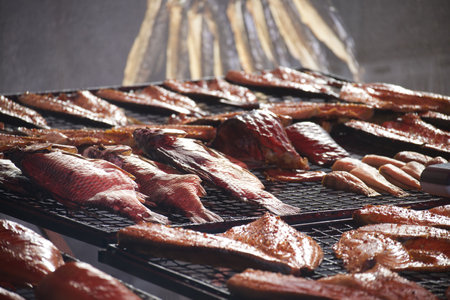 Showcasing a variety of smoked fish on a metal rack, glistening with oil and ready to be served at...