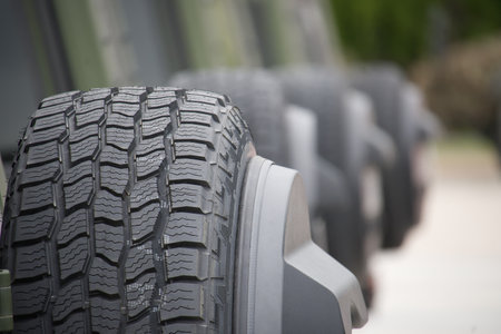 Detailed close-up view of car tires with distinct textures, arranged in a line outdoors. Ideal for...