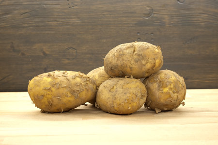 Rustic display of freshly harvested potatoes stacked on a wooden surface with an earthy background, reflecting natural produce and organic farming concepts.の写真素材