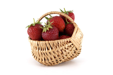 Ripe red strawberries with green stems are overflowing a small wicker basket on a white background, creating a vibrant and appetizing imageの写真素材