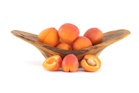 A wooden bowl overflowing with ripe, juicy apricots, some whole and others sliced open, revealing their pits.の写真素材