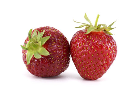 Two ripe strawberries are laying on a white surface, showcasing their vibrant red color, textured skin, and green sepals, creating a simple yet appealing compositionの写真素材