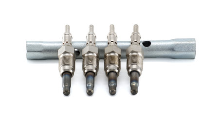 Four glow plugs rest on a wrench, against a white background, showcasing automotive engine...