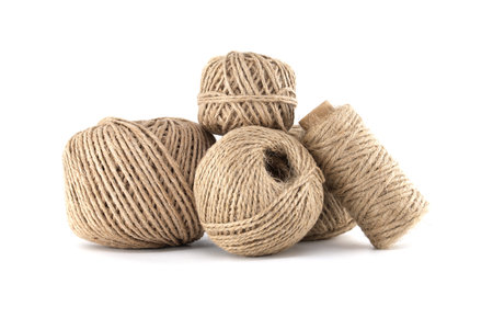 A collection of natural twine balls and a spool are arranged against a bright white background,...