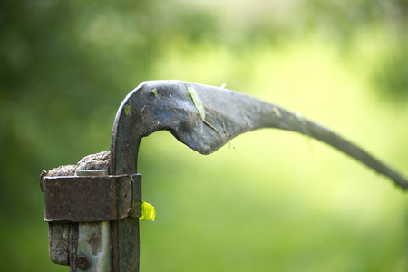 Detailed close-up of an old, rusty garden tool blade in a vibrant green outdoor setting,...
