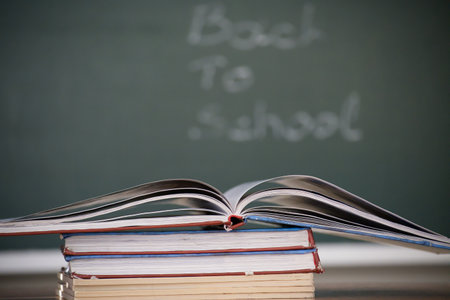 A stack of books with an open book on top against a chalkboard background with "Back to School" written on it.の写真素材