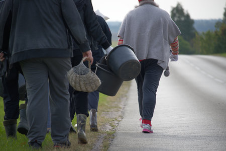 A group of people are walking along a road, carrying baskets and buckets, likely after harvesting potatoes on an organic farm. The scene suggests a rural setting.の写真素材