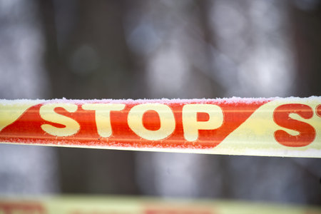 Red and yellow barrier tape stretches across snowy outdoor setting, signaling restricted area. Blurred trees in the background create cold, quiet mood and suggest caution, safety and restricted accessの写真素材