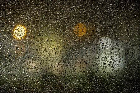 A rain-soaked window reveals scattered droplets and soft urban lights, creating a moody, atmospheric...