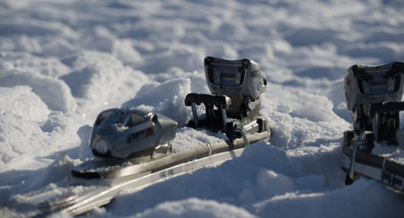 Detailed view of ski bindings partially covered in soft, white snow, illuminated by bright sunlight,...