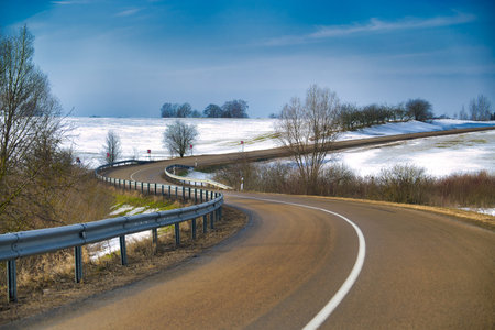 Scenic, curving highway traverses a winter countryside dotted with leafless trees and patches of...
