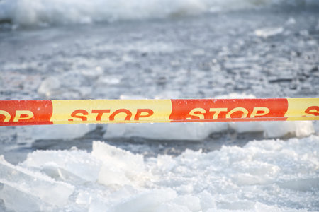 A bright yellow and red caution tape with the word STOP printed repeatedly is stretched across a...