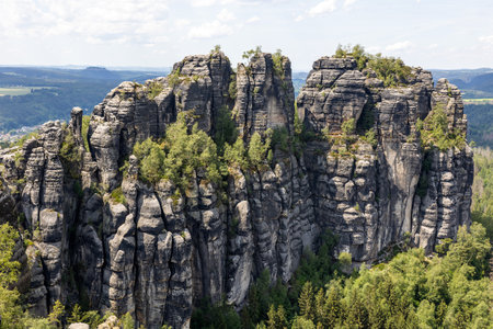 Exploring the stunning Schrammsteine rock formations in Saxon Switzerland reveals towering cliffs, lush greenery, and a breathtaking landscape under a clear blue sky.の写真素材