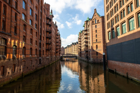 Colorful brick buildings line the calm canal in Speicherstadt, Hamburg, reflecting a bright blue sky. The area showcases the city's rich history and unique architecture.の写真素材