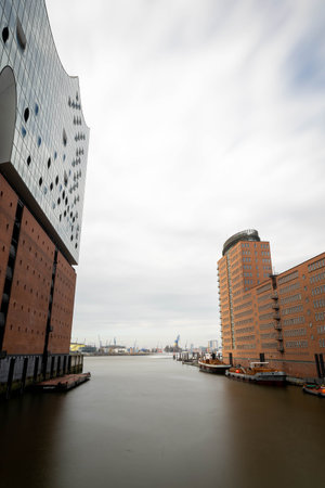 The image captures a waterfront perspective in Hamburg showing modern buildings alongside calm waters under a cloudy sky. Urban life meets architectural design in this vibrant area.の写真素材
