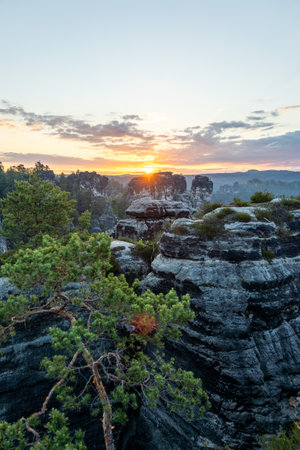 Stunning sunlight breaks over the horizon at the Bastei bridge, illuminating the rugged rock formations and lush greenery in the Elbe Sandstone Mountains of Saxony.の写真素材