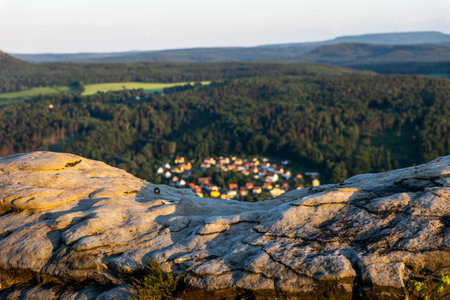 Golden hues of sunset illuminate the rugged rock formations at Lilienstein, casting a warm glow over the tranquil landscape and the nestled village below among lush greenery.の写真素材