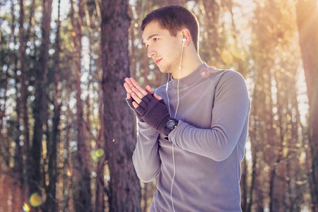 Sports man heating his hands in forest. Winter.の写真素材
