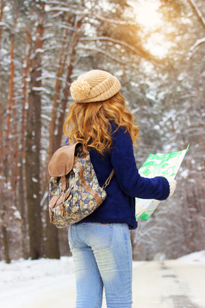 Beautiful young girl holding map in her hands, wearing blue jacket and with bag on her back. Travel girl.の写真素材