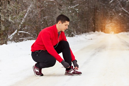 Young and handsome sportsman in red sweater ties shoelaces of his sneakers. Outdoor activity.の写真素材