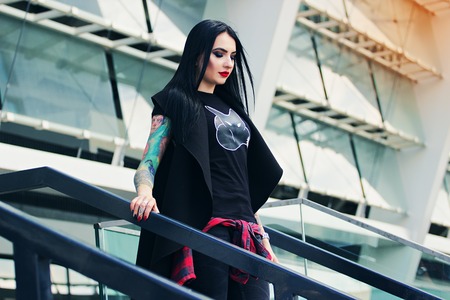 Urban gothic woman. Portrait of attractive tattoed hipster girl standing against urban background.の写真素材
