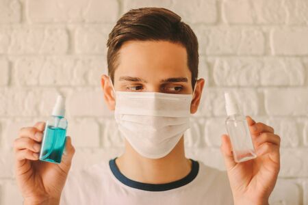 Professional doctor in protective mask on face hold sanitizer bottles in hands. Young man in medical face mask show antibacterial gel for personal safety and hygiene. Coronavirus COVID-19 protectionの写真素材