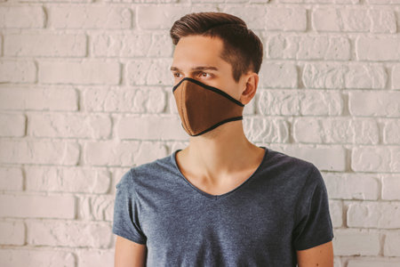 Hipster man student wearing protective face mask for protection against air pollution or coronavirus nCov-19. Young man in t-shirt wearing face mask for professional personal protection from COVID-19の写真素材