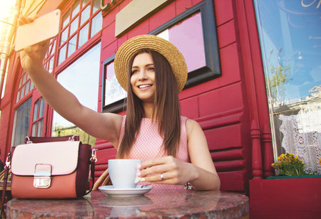 Selfie time. Portrait of vintage styled beautiful girl in hat and pink dress taking selfie while...