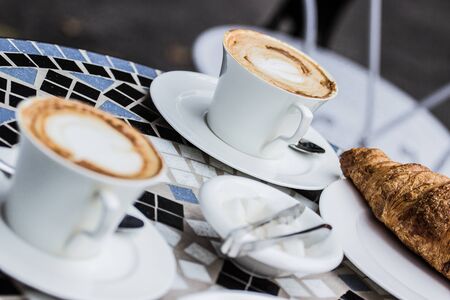 Closeup of traditional french breakfast with cups of hot coffee and fresh tasty croissants on plates placed on vintage table. French cafe. Delicious pastry. Fresh french bakery. Selective focus.の写真素材