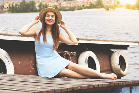 Pretty, young and attractive girl in dress spending time and posing on wooden pier. Italian fashion style.の写真素材