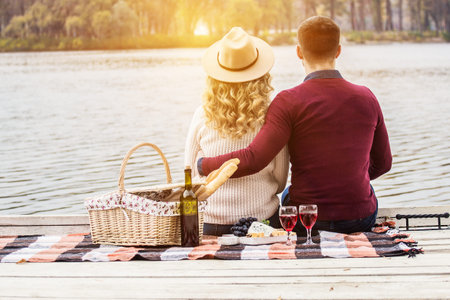 Lucky to have each other. Horizontal shot of young couple having romantic picnic and drinking wine. Man hugging his beautiful girlfriend while sitting on beach. Couple in love outdoors.の写真素材