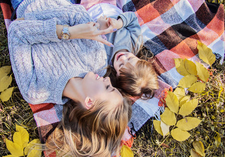 Top view young mother lying with her little daughter on blanket and smiling while having fun in...