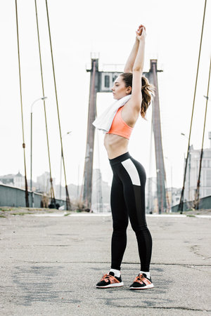 Beautiful athletic fitness girl in stylish sportswear doing stretching on bridge before morning jog....