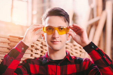 Happy man cabinet maker wearing protective glasses and smiling while working at sawmill factory....