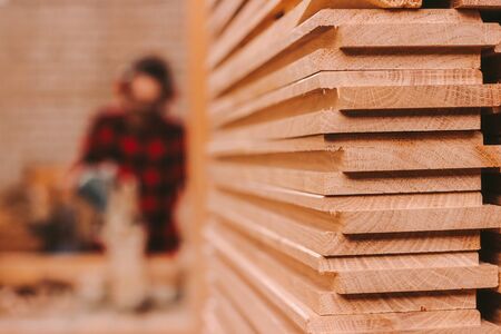 Closeup pile of wooden boards at lumber production factory. Stack of cut plywood at sawmill. Wooden material for furniture production at workshop. Carpenter using electrical circular saw on backgroundの写真素材