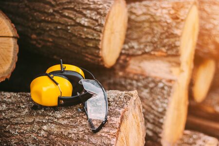 Conceptual image of protective glasses and headphones on fresh cut pine tree logs at sawmill. Professional workwear for personal protection at wood production factory. Earmuffs and protective eyewearの写真素材