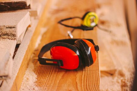 Closeup of professional protective equipment for carpenters and woodworking production workers. Protective headphones, glasses and measuring tape on joiner table. Hearing protectors, joinery workplaceの写真素材