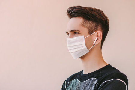 Portrait young confident fitness trainer in protective mask listening music with wireless earbuds....