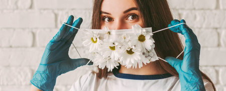 Banner young woman doctor in medical gloves wear or take off protective face mask with flowers....