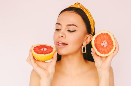 Portrait beautiful young hungry woman have fun and posing with grapefruit slices in hands isolated on white background. Happy attractive girl eat healthy citrus fruit. Beauty, fashion, diet, detoxの写真素材