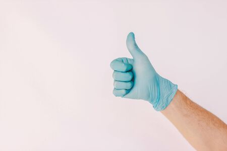 Closeup man doctor show thumb up sign with hand in medical latex glove isolated on white background. Male hand in blue protective glove gesture agreement like ok. Advice, recommend, alright, COVID-19の写真素材