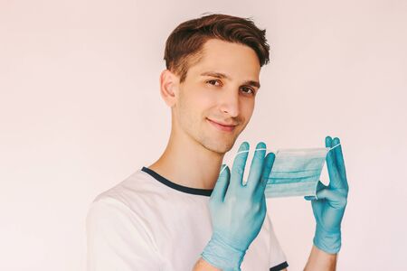 Portrait young male patient in protective gloves put on medical face mask on mouth isolated on white background. Happy man doctor nurse in medical gloves wear protective surgical mask. COVID-19 safetyの写真素材