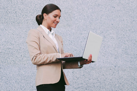 Portrait young attractive business woman in suit hold laptop in hand and smile on gray background....