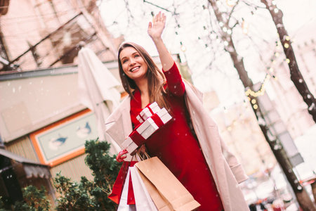 Young happy stylish woman hold shopping bags and gift boxes in hands and smile outdoors. Beautiful...