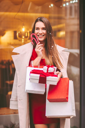 Young happy stylish woman hold shopping bags and gift boxes in hands and smile outdoors. Beautiful...
