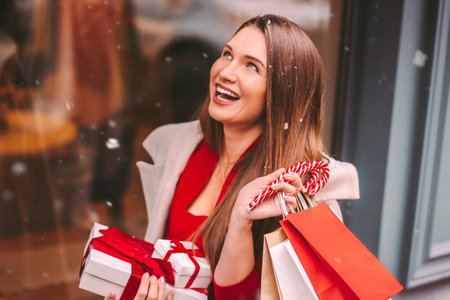 Young happy stylish woman hold shopping bags and gift boxes in hands and smile outdoors. Beautiful...