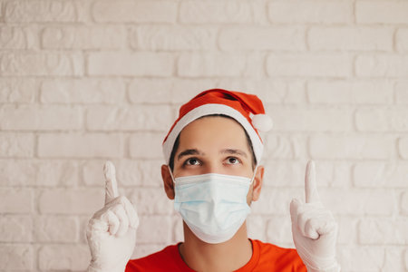 Young man courier in protective face mask, medical gloves, santa hat carry delivery boxes in hands. Happy delivery service employee in medical face mask hold cardboard packages. Christmas, New Yearの写真素材
