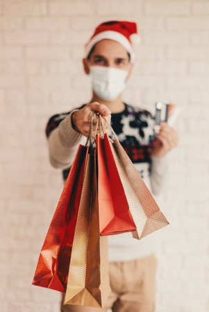 Young male doctor in Santa hat, medical face mask, protective gloves hold red heart in hands. Happy man surgeon in protective face mask show heart sign with fingers. Christmas donation, charity, helpの写真素材